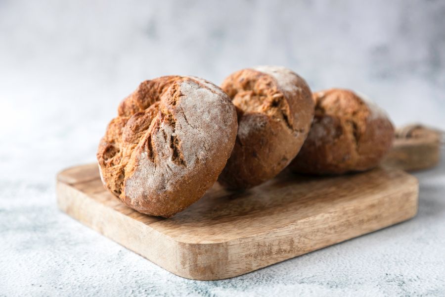 Drei frisch gebackene Roggenbrötchen auf einem Holzbrett